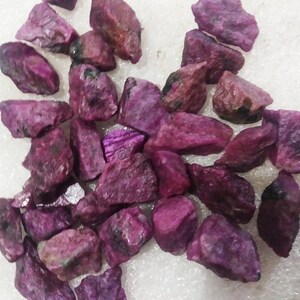 Peut inclure: Une collection de pierres précieuses rubis brutes et non polies de tailles et de formes variées. Ces pierres naturelles présentent une palette de couleurs magenta profond et rose foncé avec des textures cristallines visibles.