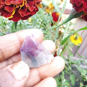 May include: A small, raw, translucent mineral specimen featuring a distinct purple and white color gradient. The stone has an irregular, jagged shape with sharp edges and a smooth, crystalline texture. The number 17 is printed in orange below.