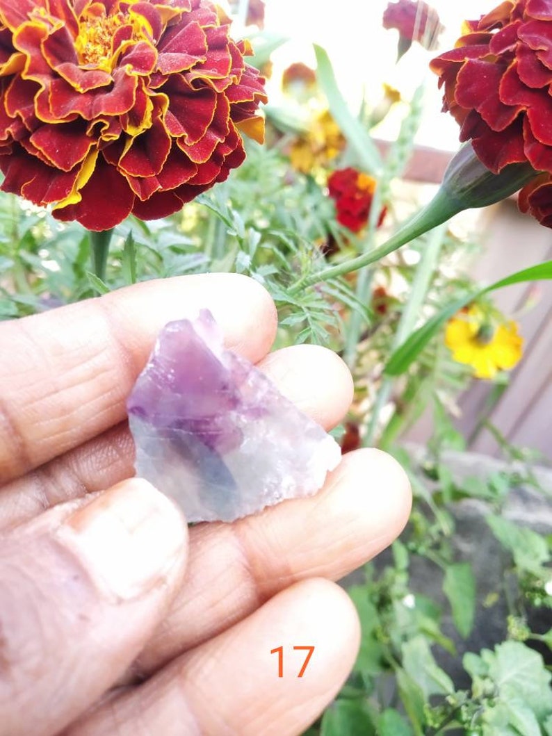 May include: A small, raw, translucent mineral specimen featuring a distinct purple and white color gradient. The stone has an irregular, jagged shape with sharp edges and a smooth, crystalline texture. The number 17 is printed in orange below.