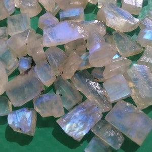 Puede incluir: Una colección de fragmentos de piedra lunar en bruto y translúcidos con una base de color blanco lechoso y destellos azules iridiscentes. Estas piezas de piedra preciosa irregulares y angulares tienen una calidad semitransparente.
