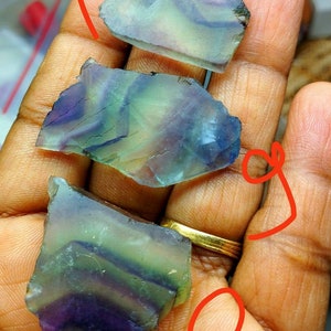 Puede incluir: Tres espec&iacute;menes minerales de fluorita irregulares y transl&uacute;cidos que presentan bandas distintivas de tonos morados, verdes y transparentes. Cada pieza muestra una superficie lisa y pulida con fracturas internas naturales y zonas de color.