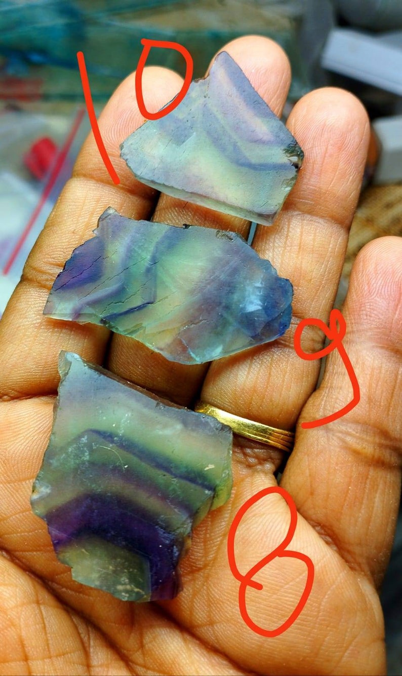 Puede incluir: Tres espec&iacute;menes minerales de fluorita irregulares y transl&uacute;cidos que presentan bandas distintivas de tonos morados, verdes y transparentes. Cada pieza muestra una superficie lisa y pulida con fracturas internas naturales y zonas de color.