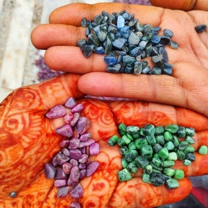 Può includere: Una collezione di piccole pietre preziose levigate tenute nei palmi delle mani. Un palmo contiene un gruppo di pietre blu scuro, mentre l'altro palmo contiene due mucchi separati di piccole pietre levigate: una è rosa magenta e l'altra verde brillante.