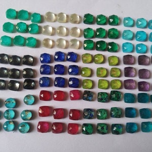 May include: A collection of small, faceted gemstones arranged in a grid. The stones are square and round, featuring a variety of colors including teal, white, green, blue, black, yellow, purple, red, and turquoise with metallic gold veining.