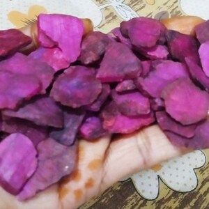 May include: A collection of small, irregular, flat, and vibrant magenta-colored stone slices. Each piece features a rough, textured surface with varying shades of deep pink and purple, displaying natural edges and a matte finish throughout the group.