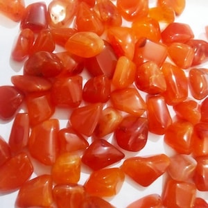 Op de afbeelding: Een verzameling getrommelde carneoolstenen in verschillende tinten oranje, rood en diep amber. Elke steen heeft een glad, gepolijst oppervlak met een doorschijnende kwaliteit en vertoont natuurlijke variaties in kleur en vorm.