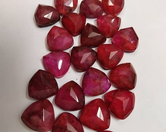 May include: A collection of loose, faceted gemstones in a deep red color. Each stone features a triangular shape with multiple flat, polished surfaces that reflect light. The stones vary slightly in their shade of red, ranging from dark crimson to bright magenta, and are arranged in a scattered pattern.