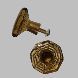 May include: Two amber glass cabinet knobs with a geometric pattern. The knobs have a brass base and a screw for attaching to a cabinet door.