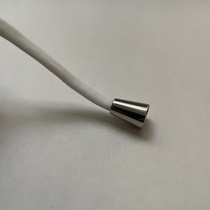 May include: A white cord with a silver metal tip. The tip is shaped like a cone.