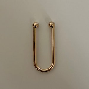 May include: A gold-colored metal key ring with rounded ends. The ring is shaped like a U.