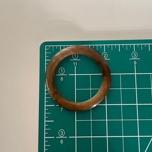 May include: A brown and white ring-shaped object with a smooth surface. The object is approximately 2 inches in diameter and is lying on a green cutting mat.