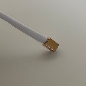 Könnte beinhalten: Ein weißes Kabel mit einer goldfarbenen Metallspitze.