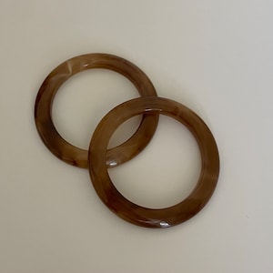 Peut inclure: Deux anneaux en plastique marbré brun et blanc. Les anneaux sont entrelacés et mesurent environ 7,5 cm de diamètre.