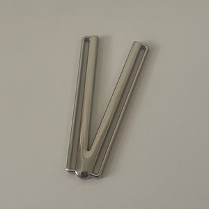 May include: Silver metal buckle with a V-shaped design. The buckle has two parallel slots on each side.