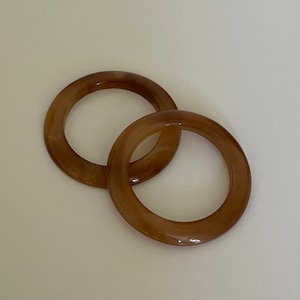 Puede incluir: Dos anillos de plástico marrón con un patrón de mármol. Los anillos están entrelazados.