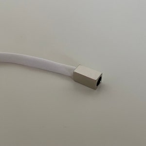 Puede incluir: Un cordón blanco con una tapa de extremo de metal plateado. La tapa tiene un pequeño agujero en el centro.