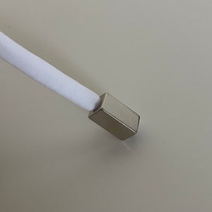 Könnte beinhalten: Ein weißes Kabel mit einer silbernen Metallendkappe. Das Kabel ist an einem Metallobjekt befestigt.