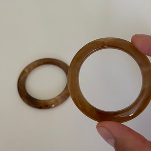 May include: Two brown plastic rings with a marbled pattern. The rings are about 3 inches in diameter.