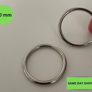 Könnte beinhalten: Zwei silberne Metallringe, jeder mit einem Durchmesser von 30 mm. Die Ringe liegen auf einer weißen Oberfläche.