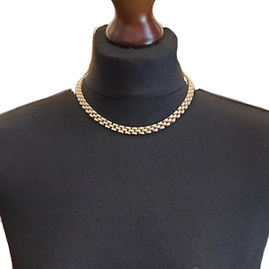 May include: A gold chain necklace on a black mannequin bust. The chain is made of interlocking links.