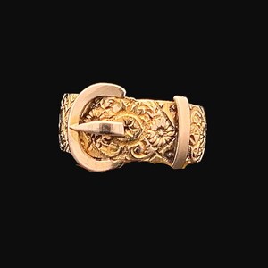 May include: A gold-toned ring featuring an intricate buckle design. The ring is crafted from metal and has a polished finish.