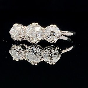 Puede incluir: Un anillo de diamantes de tres piedras con una banda de oro blanco. Los diamantes son redondos y de talla brillante.