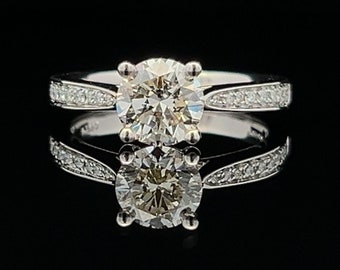 May include: A silver engagement ring with a round, clear diamond center stone and a band of smaller diamonds.