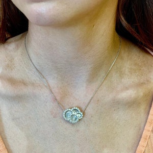 Puede incluir: Un collar de cadena de plata con un colgante que presenta un grupo de pequeñas piedras redondas y transparentes engastadas en un marco de plata.