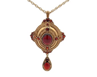 May include: A gold pendant necklace with a red gemstone in the center. The pendant is surrounded by smaller red gemstones and has a teardrop-shaped pendant hanging from it.