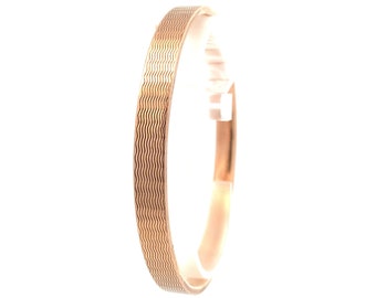 May include: A rose gold bangle bracelet with a wavy, textured pattern. The bracelet is a simple, elegant design, suitable for everyday wear. The metal has a warm, polished finish, reflecting light.