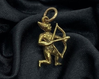 May include: A gold-colored pendant in the shape of a kneeling archer, with a bow and arrow, in a black velvet box.