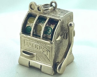 May include: Gold-toned charm shaped like a slot machine with a lever and the word "JACKPOT" on the front. The wheels have red, green, and yellow colors.