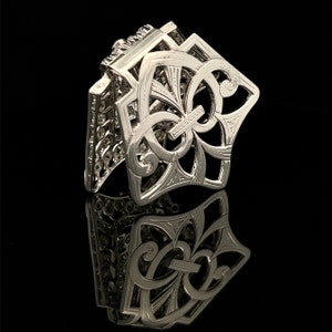 May include: A silver filigree hair clip with a decorative floral design. The clip is open and ready to be used.