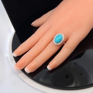 May include: A turquoise oval gemstone ring with a halo of small diamonds set in white gold.