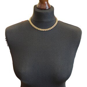 May include: A gold chain necklace on a black mannequin bust. The chain is made of interlocking links.