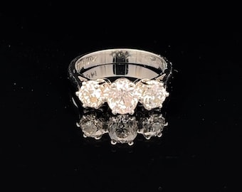 May include: A silver ring with three round, clear gemstones. The ring is set on a black surface, and the gemstones reflect light. The ring is a classic design, suitable for various occasions.