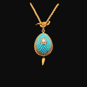Op de afbeelding: Een gouden ketting met een turquoise en parel hanger. De hanger is eivormig met een stervormig ontwerp in het midden.
