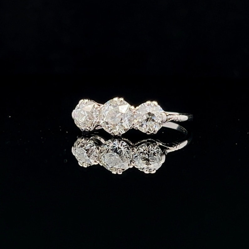 Puede incluir: Un anillo de diamantes de tres piedras con una banda de oro blanco. Los diamantes son redondos y de talla brillante.