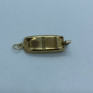 May include: A gold-toned metal charm in the shape of a small boat with a textured surface and a loop for attaching to a necklace or bracelet.