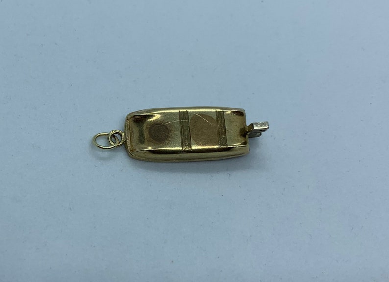 May include: A gold-toned metal charm in the shape of a small boat with a textured surface and a loop for attaching to a necklace or bracelet.