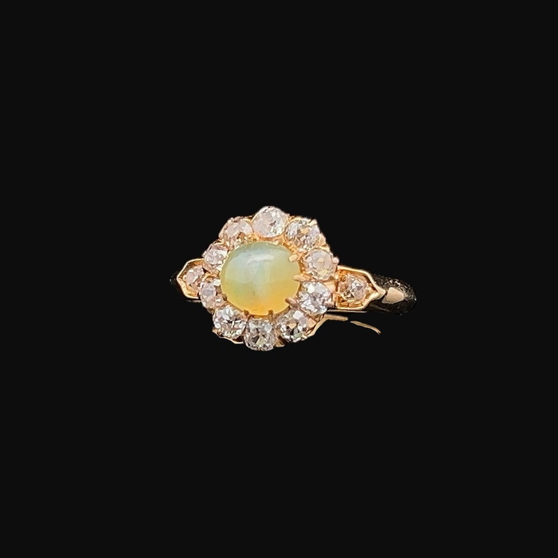 May include: A gold ring with a green opal gemstone surrounded by a halo of small diamonds.