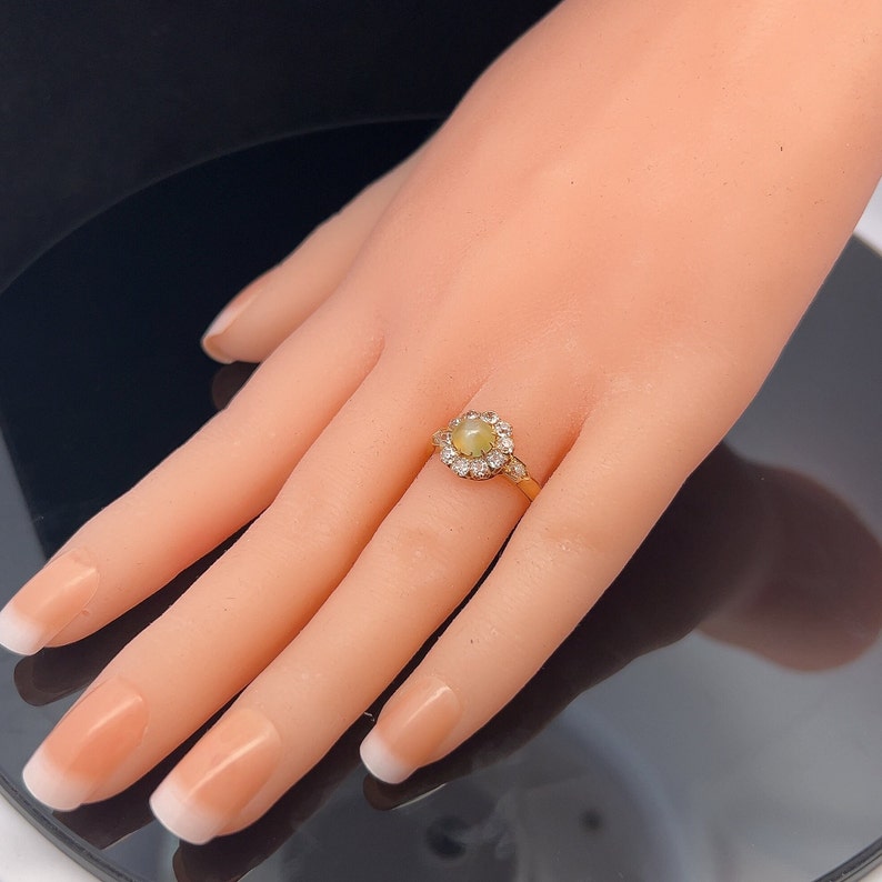 May include: A gold ring with a round, light green gemstone surrounded by a halo of smaller diamonds.