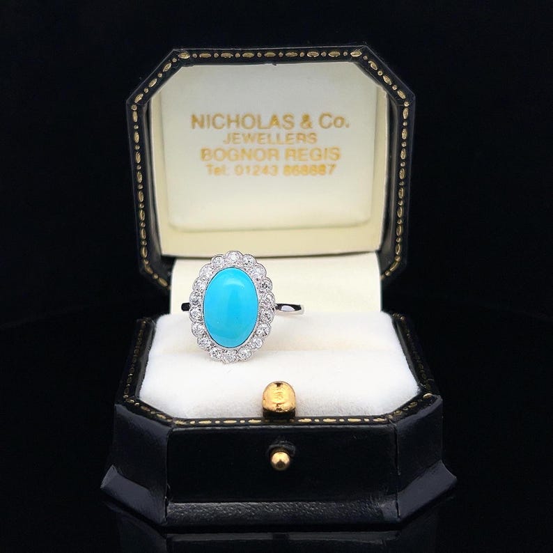 May include: A turquoise gemstone ring with a halo of diamonds set in white gold. The ring is in a black ring box with the name "Nicholas & Co. Jewellers Bognor Regis Tel 01243 860887" printed on the inside.