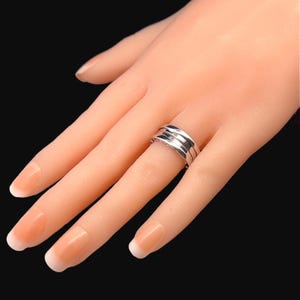 May include: A silver ring with three bands, each with a slightly different texture. The ring is worn on a model's finger.
