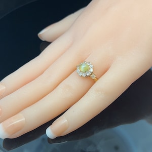 May include: A gold ring with a round, light green gemstone surrounded by smaller clear gemstones.