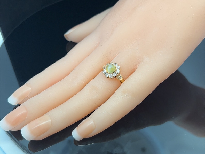 May include: A gold ring with a round, light green gemstone surrounded by smaller clear gemstones.