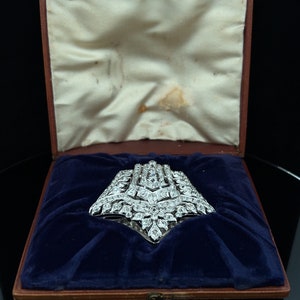 May include: A large, diamond-encrusted brooch in a silver setting, displayed in a blue velvet-lined box.