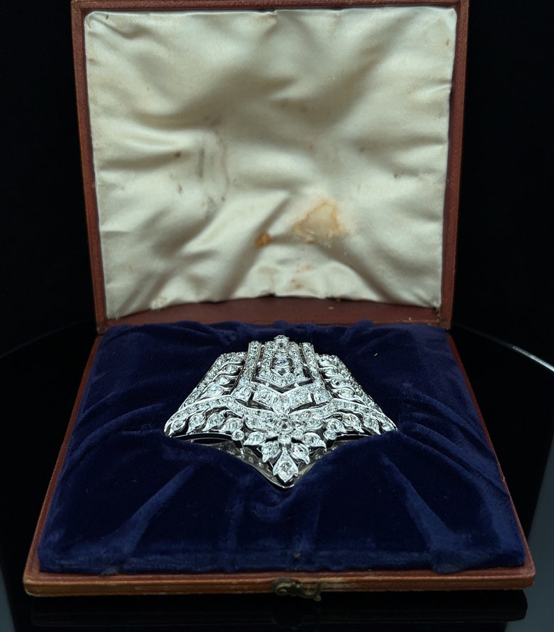 May include: A large, diamond-encrusted brooch in a silver setting, displayed in a blue velvet-lined box.