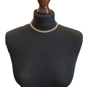 May include: A gold chain necklace on a black mannequin bust. The necklace is made of small, linked oval shapes.