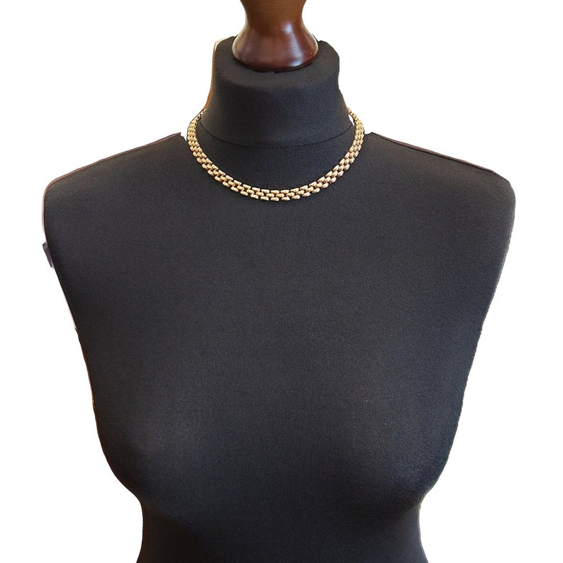 May include: A gold chain necklace on a black mannequin bust. The chain is made of interlocking links.
